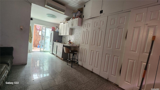 kitchen featuring decorative backsplash, stainless steel fridge, white cabinetry, and a wall mounted AC