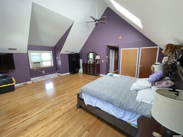 bedroom featuring high vaulted ceiling, a skylight, light hardwood / wood-style flooring, and multiple closets