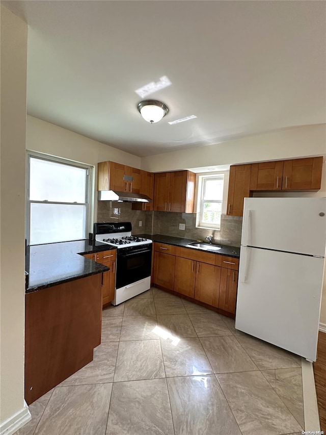 kitchen with dark countertops, freestanding refrigerator, brown cabinets, and gas stove