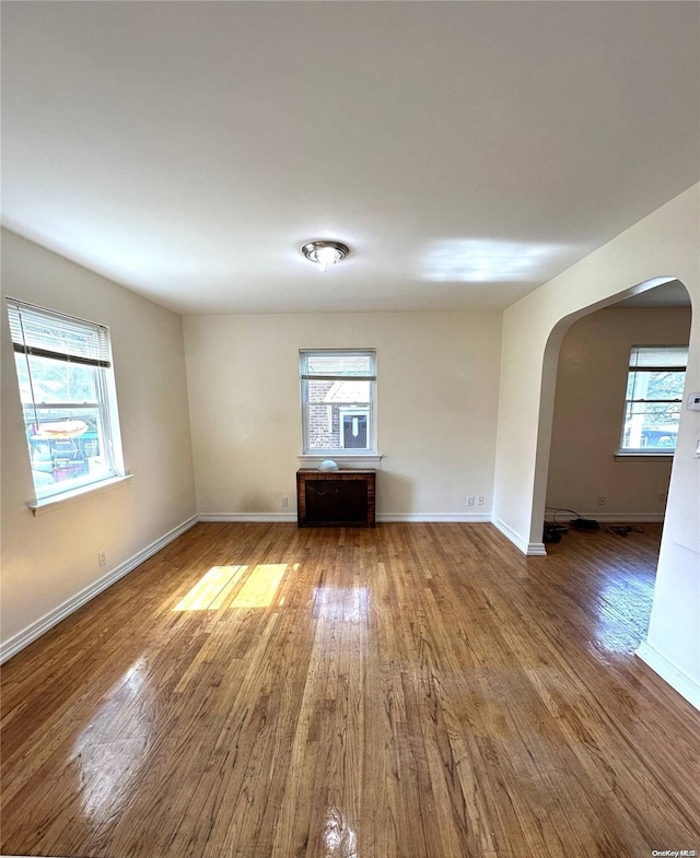 spare room featuring arched walkways, baseboards, and wood finished floors