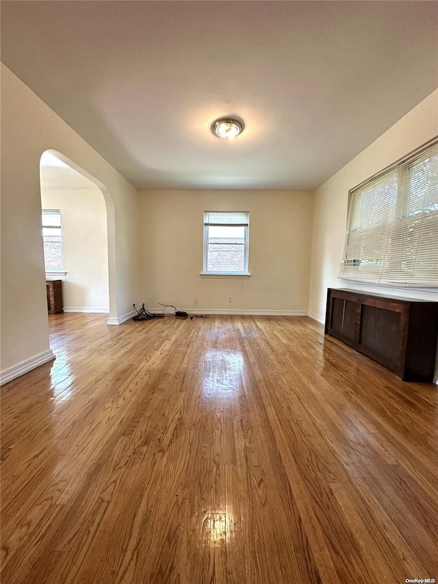 unfurnished living room with arched walkways, light wood-style flooring, and baseboards