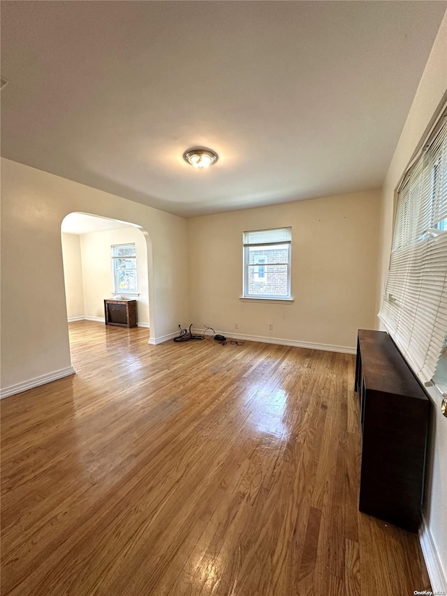 empty room featuring arched walkways, wood finished floors, and baseboards