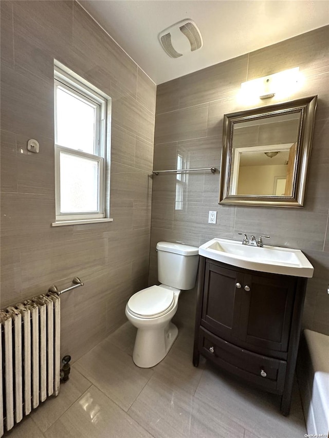 bathroom with toilet, vanity, tile walls, tile patterned floors, and radiator heating unit