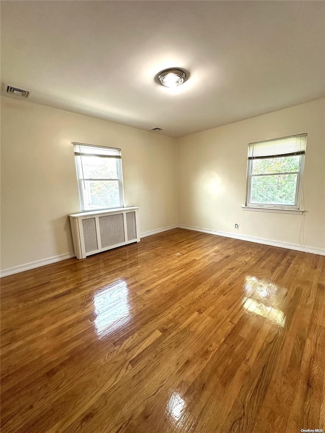 empty room with plenty of natural light, radiator heating unit, and wood finished floors