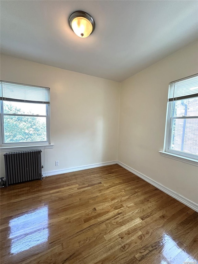 unfurnished room featuring a healthy amount of sunlight, wood finished floors, and radiator