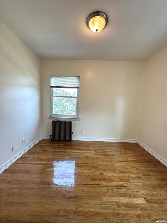 unfurnished room with radiator, baseboards, and wood finished floors