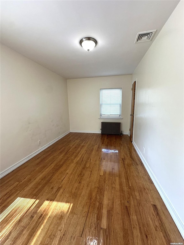 empty room with radiator, visible vents, baseboards, and wood finished floors