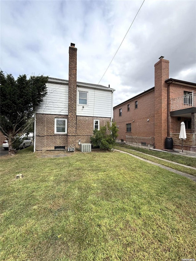 back of house with brick siding, a lawn, a chimney, and cooling unit