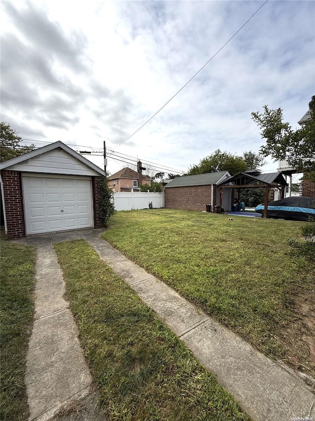 view of yard featuring driveway, a detached garage, fence, and an outbuilding