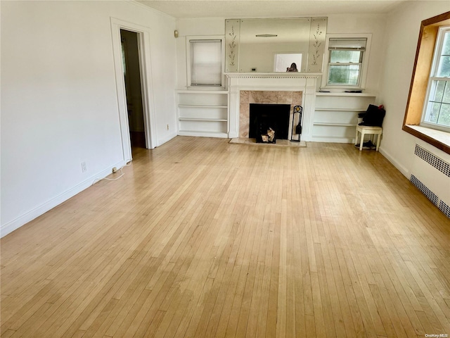 unfurnished living room featuring built in shelves, a fireplace, radiator, and light hardwood / wood-style flooring