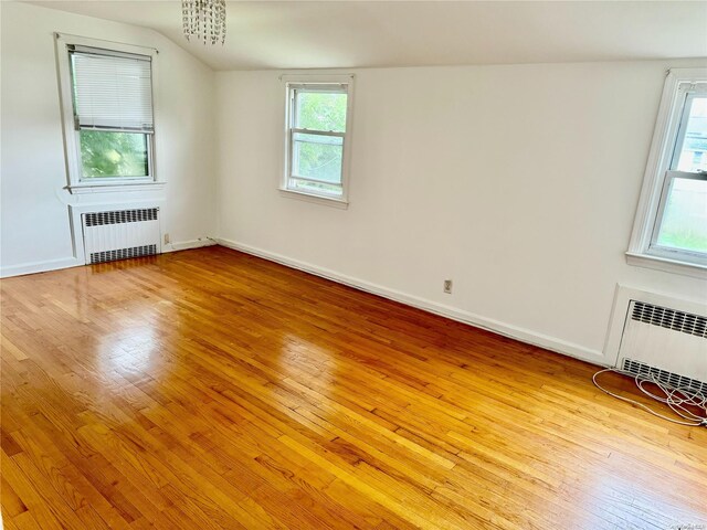 empty room with plenty of natural light, lofted ceiling, radiator, and light hardwood / wood-style flooring