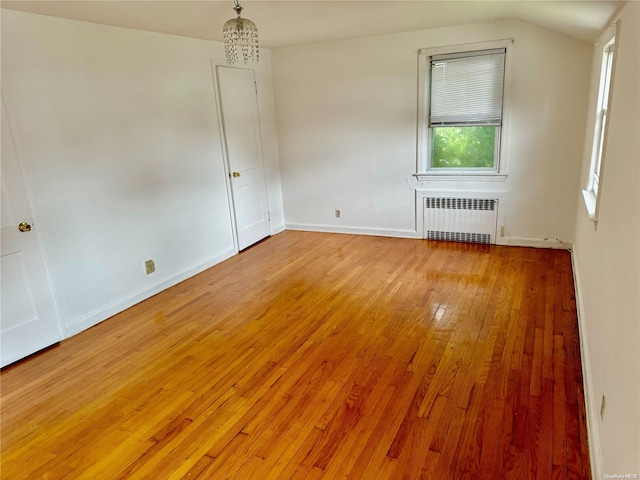 empty room with hardwood / wood-style flooring, vaulted ceiling, and radiator