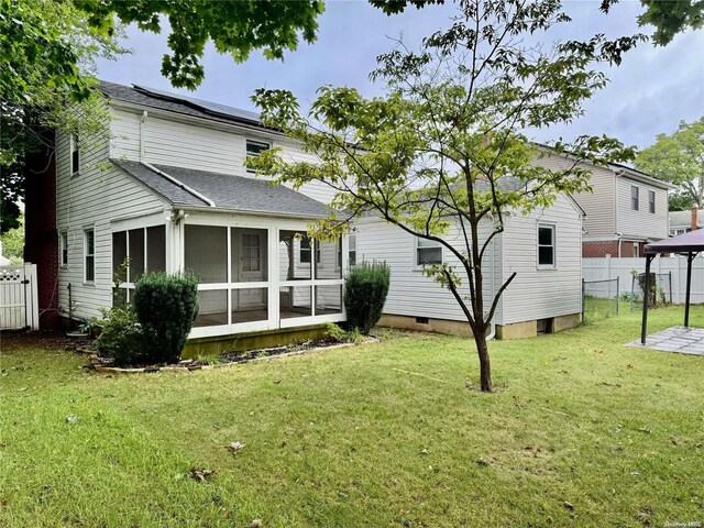 back of property featuring solar panels, a yard, and a sunroom