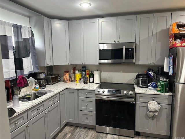 kitchen featuring gray cabinetry, sink, stainless steel appliances, light stone counters, and light wood-type flooring