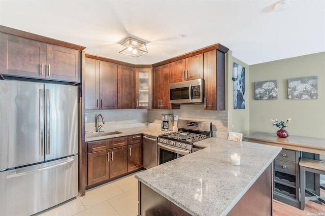 kitchen featuring kitchen peninsula, stainless steel appliances, tasteful backsplash, light stone counters, and sink