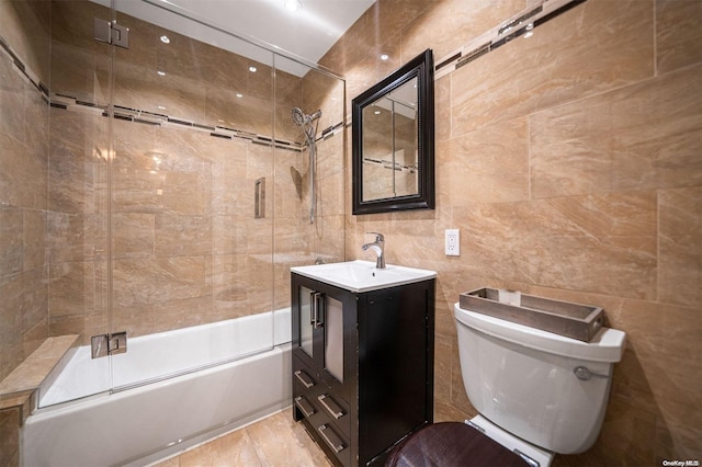 full bathroom featuring toilet, combined bath / shower with glass door, tile walls, and vanity