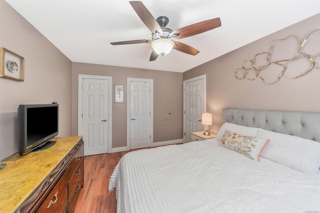 bedroom with ceiling fan, two closets, and hardwood / wood-style floors