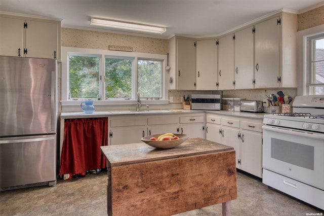 kitchen with decorative backsplash, stainless steel fridge, ornamental molding, sink, and white stove