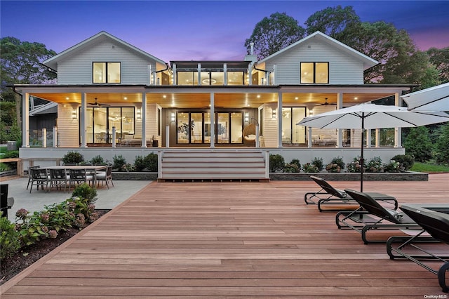 back house at dusk with a wooden deck and ceiling fan