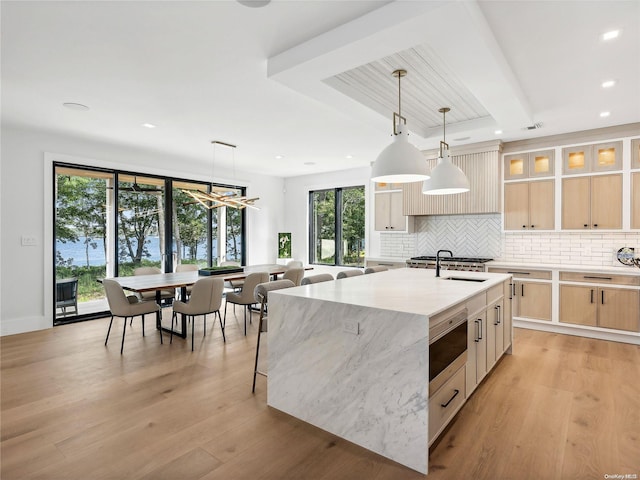 kitchen with light brown cabinets, pendant lighting, a center island with sink, and light hardwood / wood-style floors