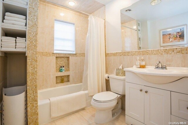 full bathroom featuring tile patterned flooring, tile walls, toilet, vanity, and shower / tub combo