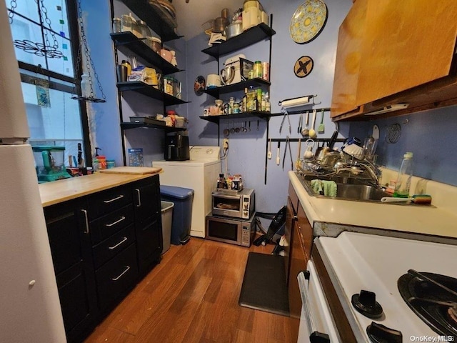 kitchen with white stove, washer and clothes dryer, dark hardwood / wood-style floors, and sink