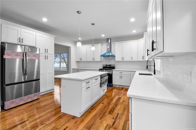 kitchen with sink, wall chimney range hood, a kitchen island, white cabinets, and appliances with stainless steel finishes