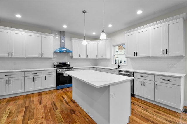 kitchen featuring appliances with stainless steel finishes, wall chimney range hood, light hardwood / wood-style flooring, white cabinets, and a kitchen island