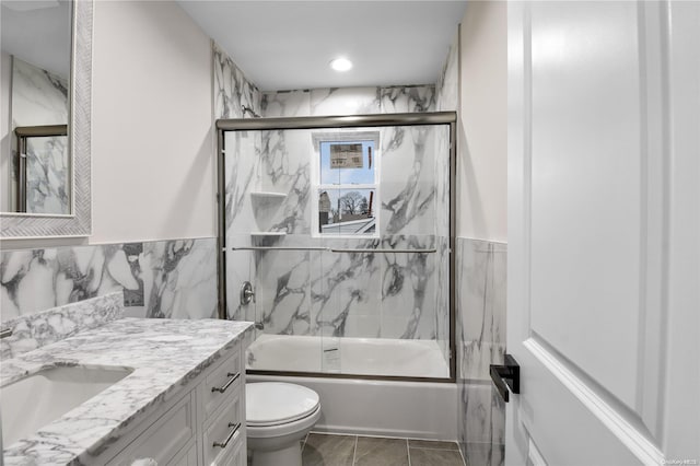 full bathroom featuring vanity, toilet, bath / shower combo with glass door, and tile walls