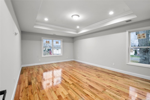 spare room with a raised ceiling, crown molding, and light wood-type flooring