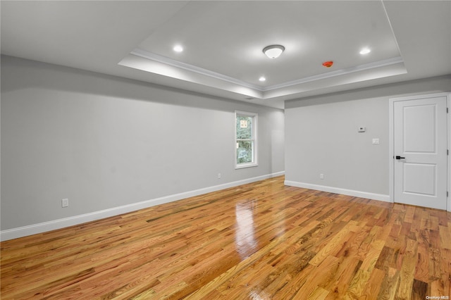 empty room with light wood-type flooring, crown molding, and a tray ceiling