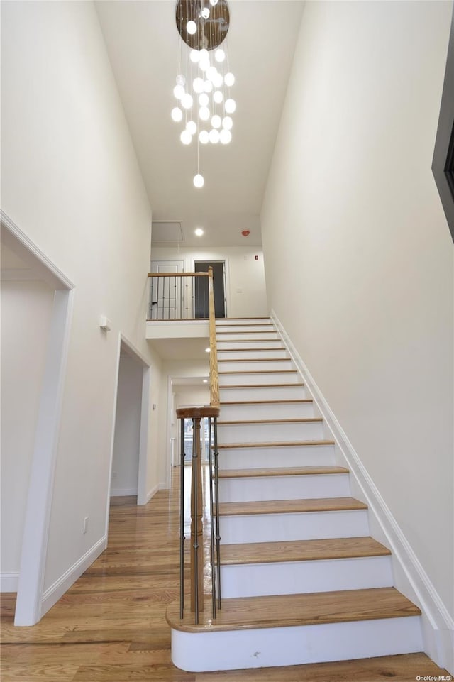 stairs featuring a chandelier, wood-type flooring, and a high ceiling