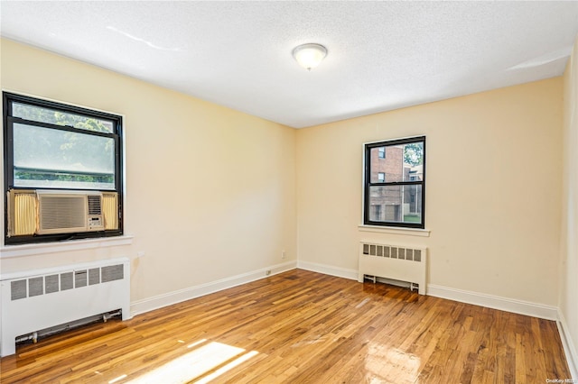 spare room featuring radiator heating unit, light hardwood / wood-style flooring, and a wealth of natural light