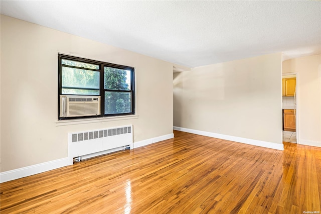 empty room with cooling unit, a textured ceiling, radiator, and light hardwood / wood-style flooring