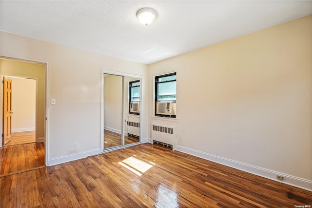 unfurnished bedroom with hardwood / wood-style flooring, cooling unit, radiator heating unit, and a closet