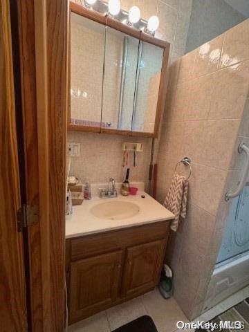 bathroom with tile patterned floors, vanity, a shower, and tile walls