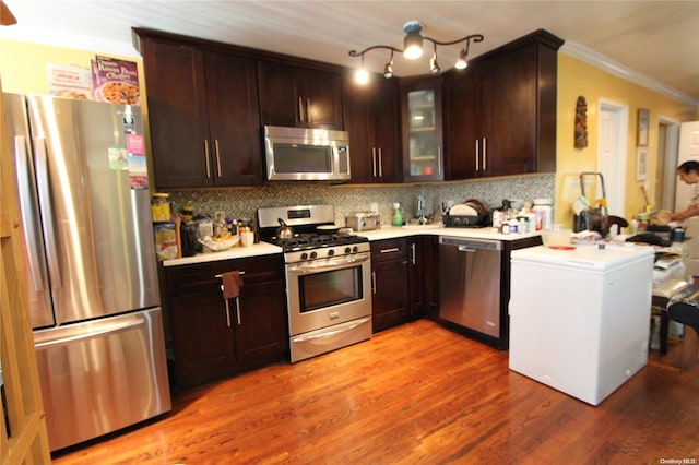 kitchen with appliances with stainless steel finishes, backsplash, crown molding, and wood-type flooring