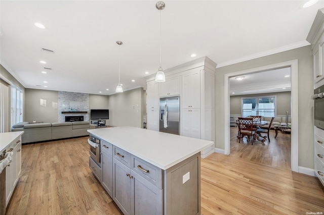 kitchen featuring light wood-type flooring, stainless steel appliances, decorative light fixtures, white cabinetry, and a stone fireplace