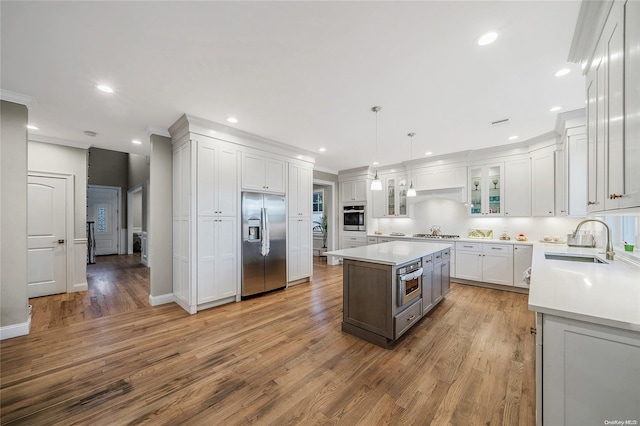 kitchen with sink, stainless steel appliances, a kitchen island, pendant lighting, and white cabinets