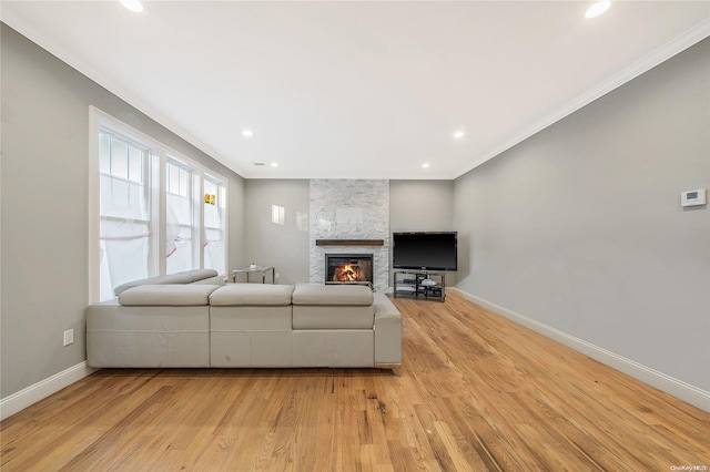 living room featuring a stone fireplace, crown molding, and light wood-type flooring