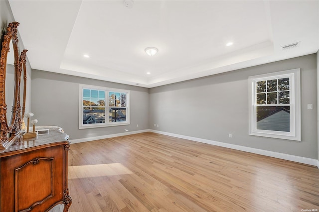 unfurnished living room with light wood-type flooring and a raised ceiling