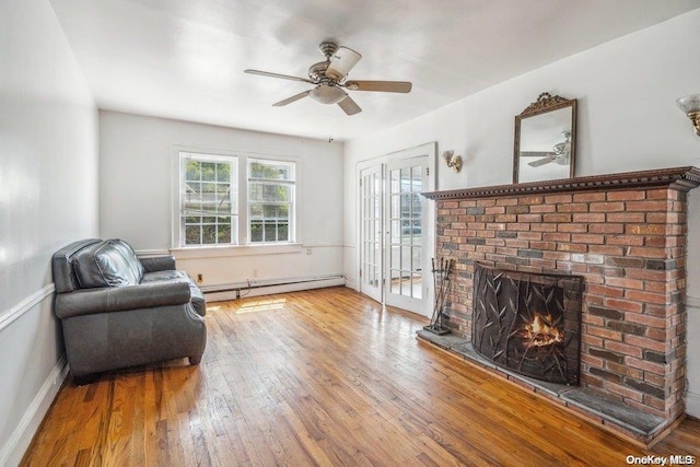 living area featuring hardwood / wood-style flooring, ceiling fan, a brick fireplace, and a baseboard radiator