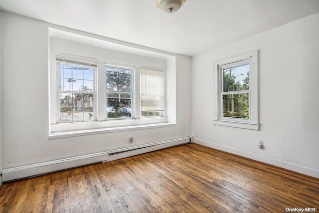 unfurnished room featuring hardwood / wood-style floors and a baseboard heating unit