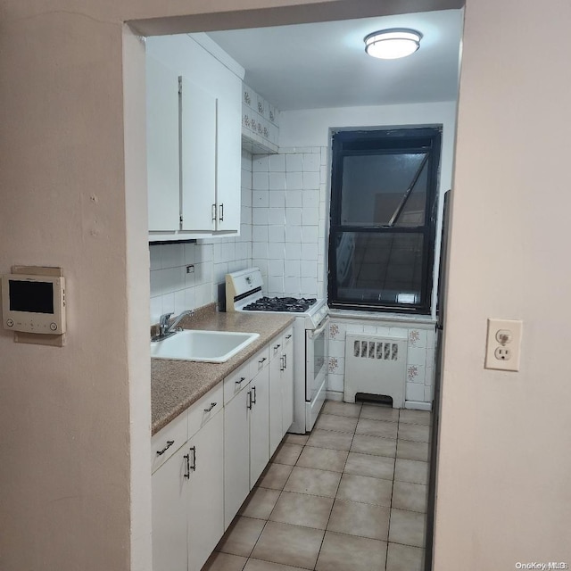 kitchen featuring decorative backsplash, radiator, gas range gas stove, sink, and white cabinetry