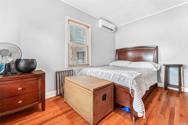 bedroom with an AC wall unit, radiator heating unit, and light hardwood / wood-style floors