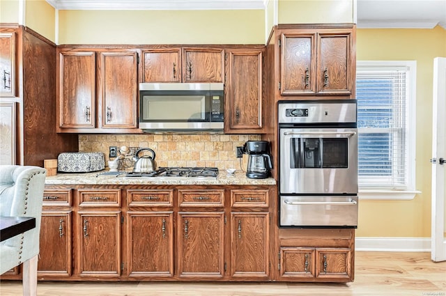 kitchen featuring crown molding, light wood-type flooring, appliances with stainless steel finishes, tasteful backsplash, and light stone counters