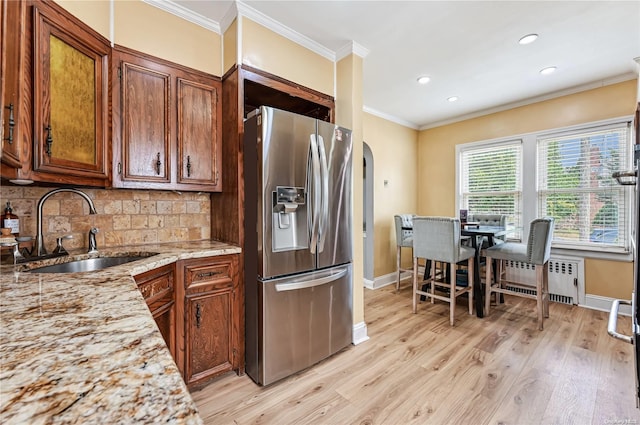 kitchen with stainless steel fridge, light wood-type flooring, light stone counters, radiator, and sink