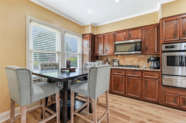 kitchen featuring decorative backsplash, crown molding, light wood-type flooring, and appliances with stainless steel finishes