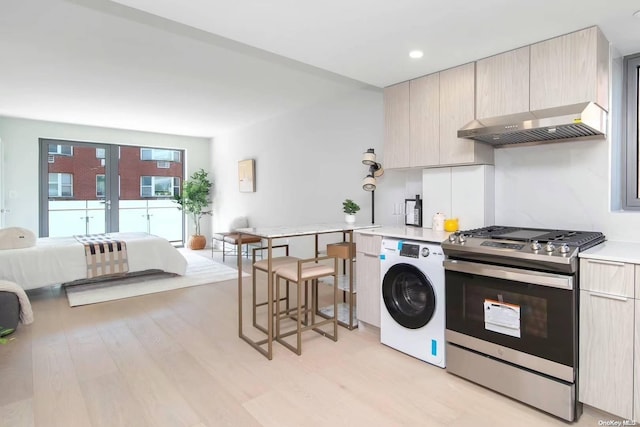 kitchen with gas range, washer / dryer, light brown cabinetry, exhaust hood, and light wood-type flooring