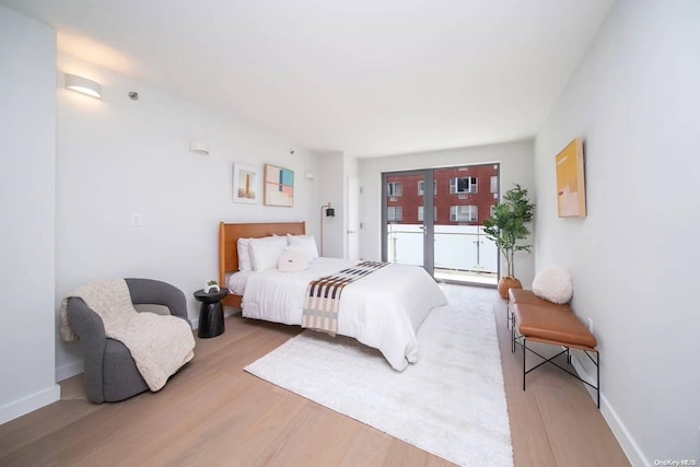 bedroom with light hardwood / wood-style floors, access to outside, and a baseboard heating unit